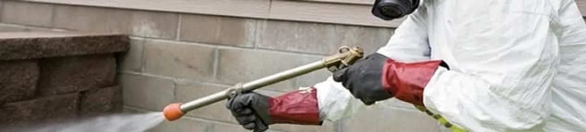 Pest control technician applying exterior insect treatment along a home foundation in Philadelphia, PA