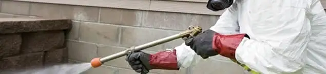 Pest control technician applying exterior insect treatment along a home foundation in Philadelphia, PA