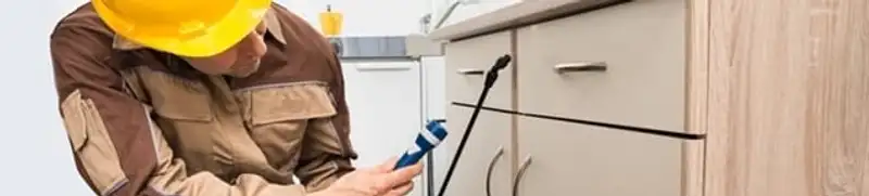 Roach exterminator applying treatment under kitchen cabinets in Philadelphia, PA
