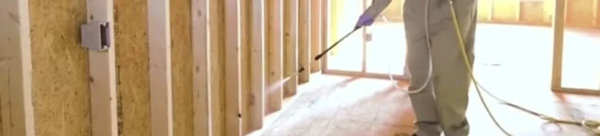 Termite treatment technician applying spray along framing and unfinished walls in Philadelphia, PA