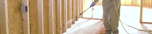 Termite treatment technician applying spray along framing and unfinished walls in Philadelphia, PA